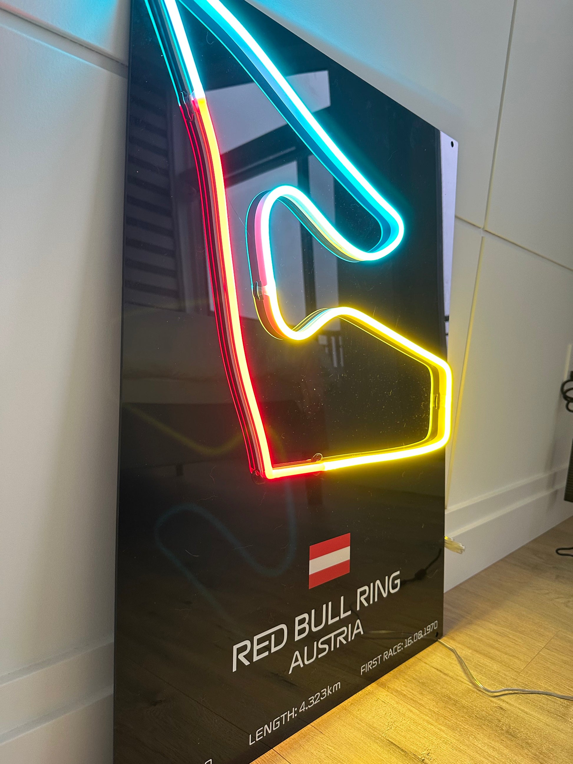 Neon sign of a race track with Red Bull Ring Austria branding on a dark background.