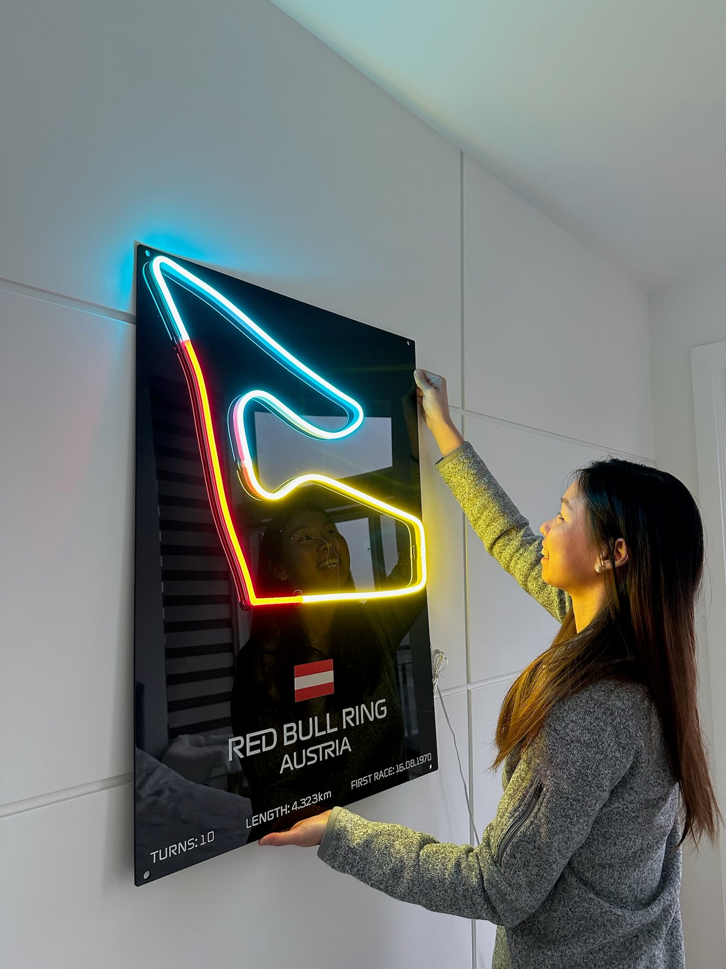 Person interacting with a neon sign of Red Bull Ring Austria on a white wall.