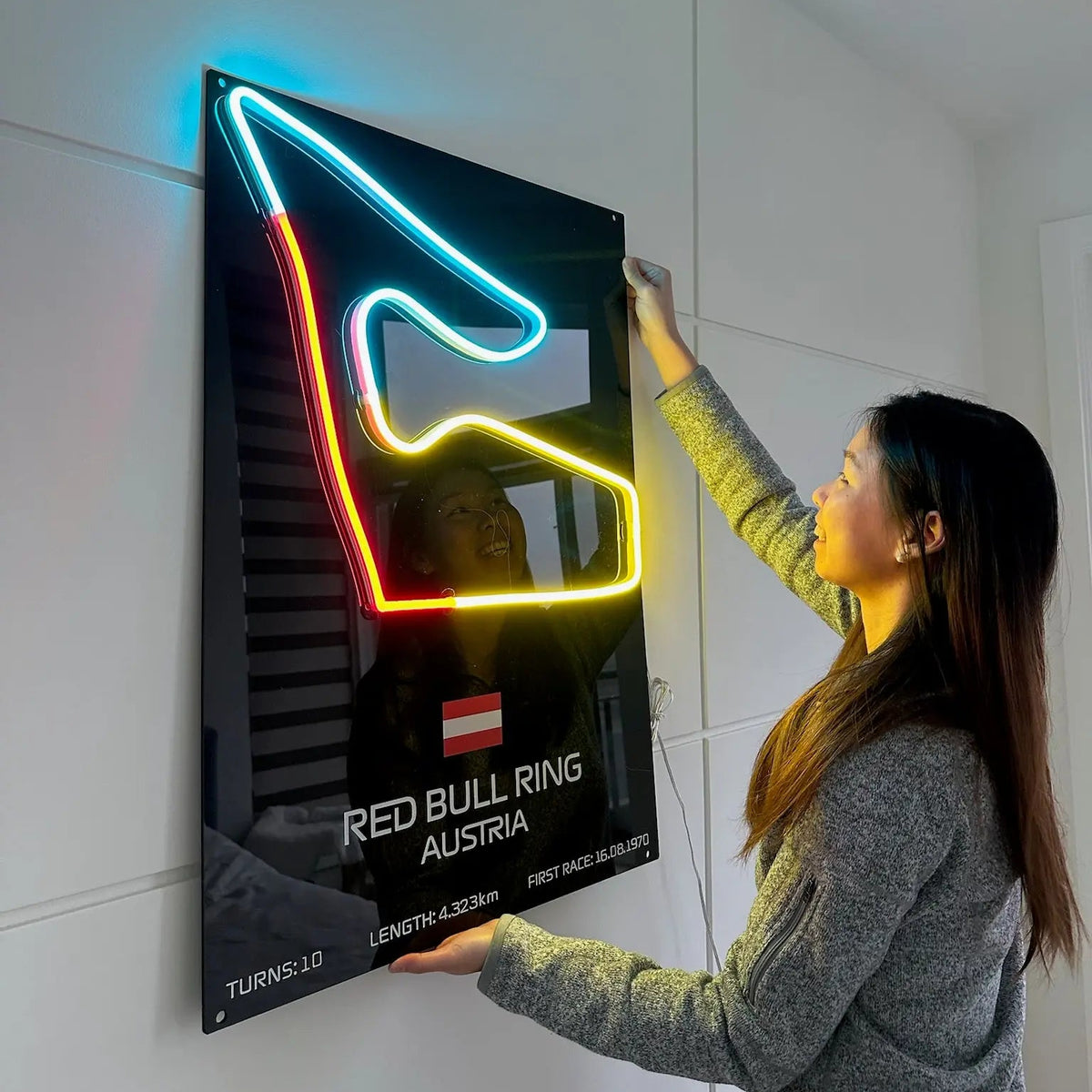 Person interacting with a neon sign of Red Bull Ring Austria on a white wall.