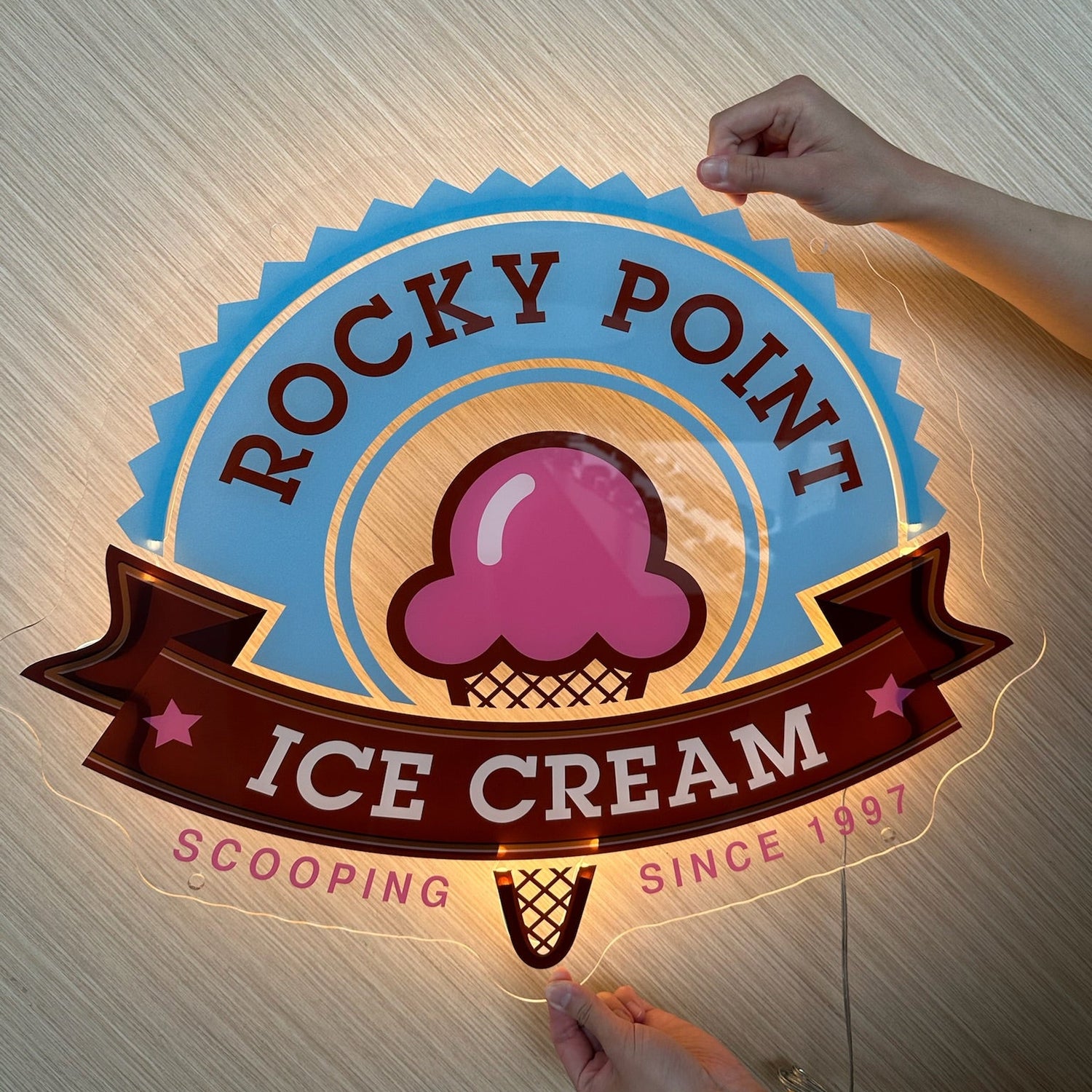Rocky Point Ice Cream sign with a hand holding it against a textured wall.
