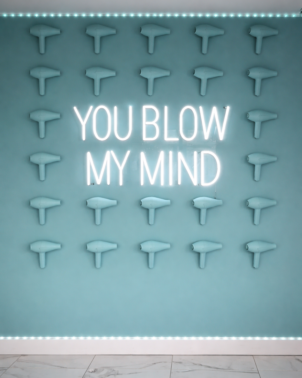 Neon sign with 'YOU BLOW MY MIND' text on a wall with hair dryers.