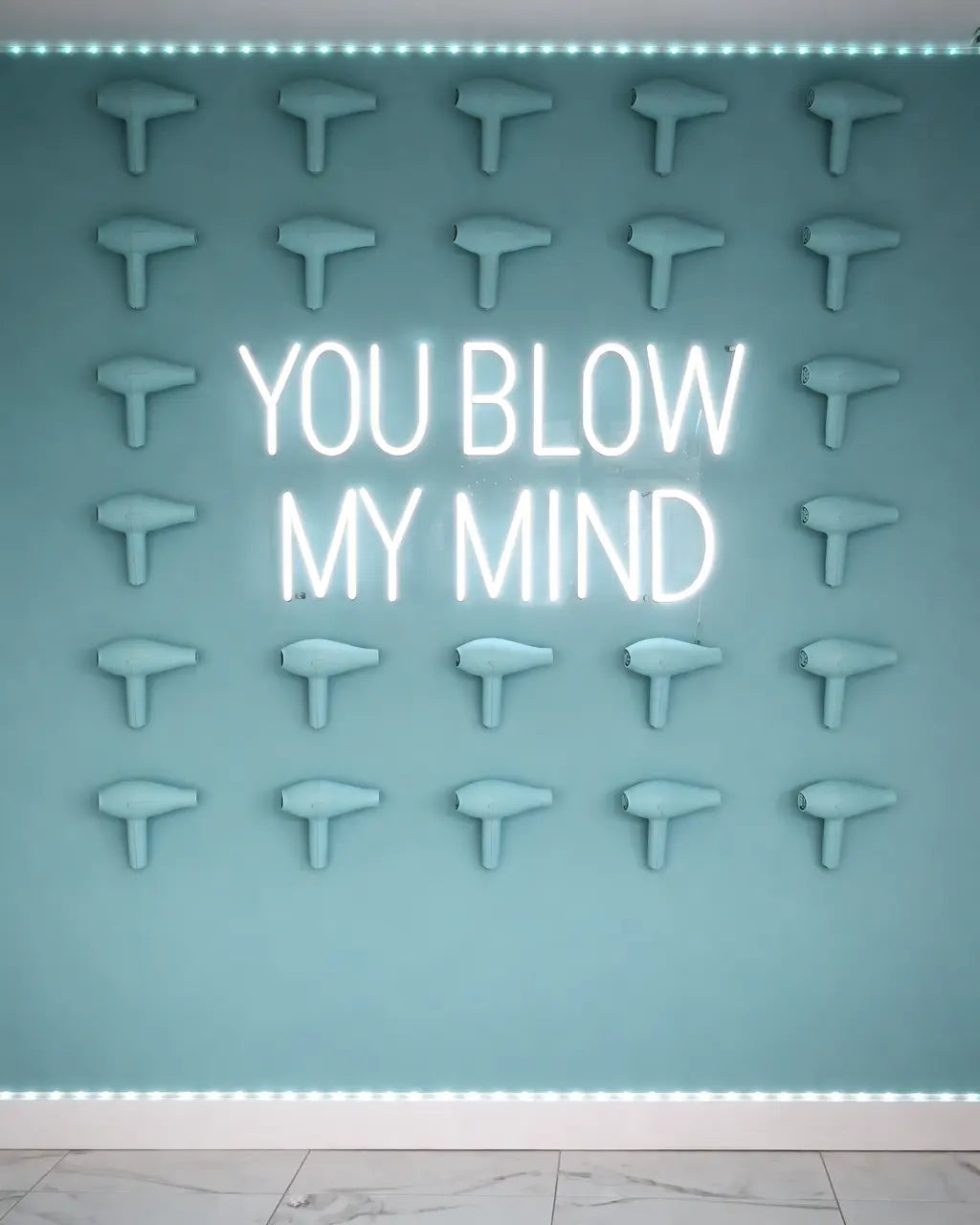 Neon sign with 'YOU BLOW MY MIND' text on a wall with hair dryers.