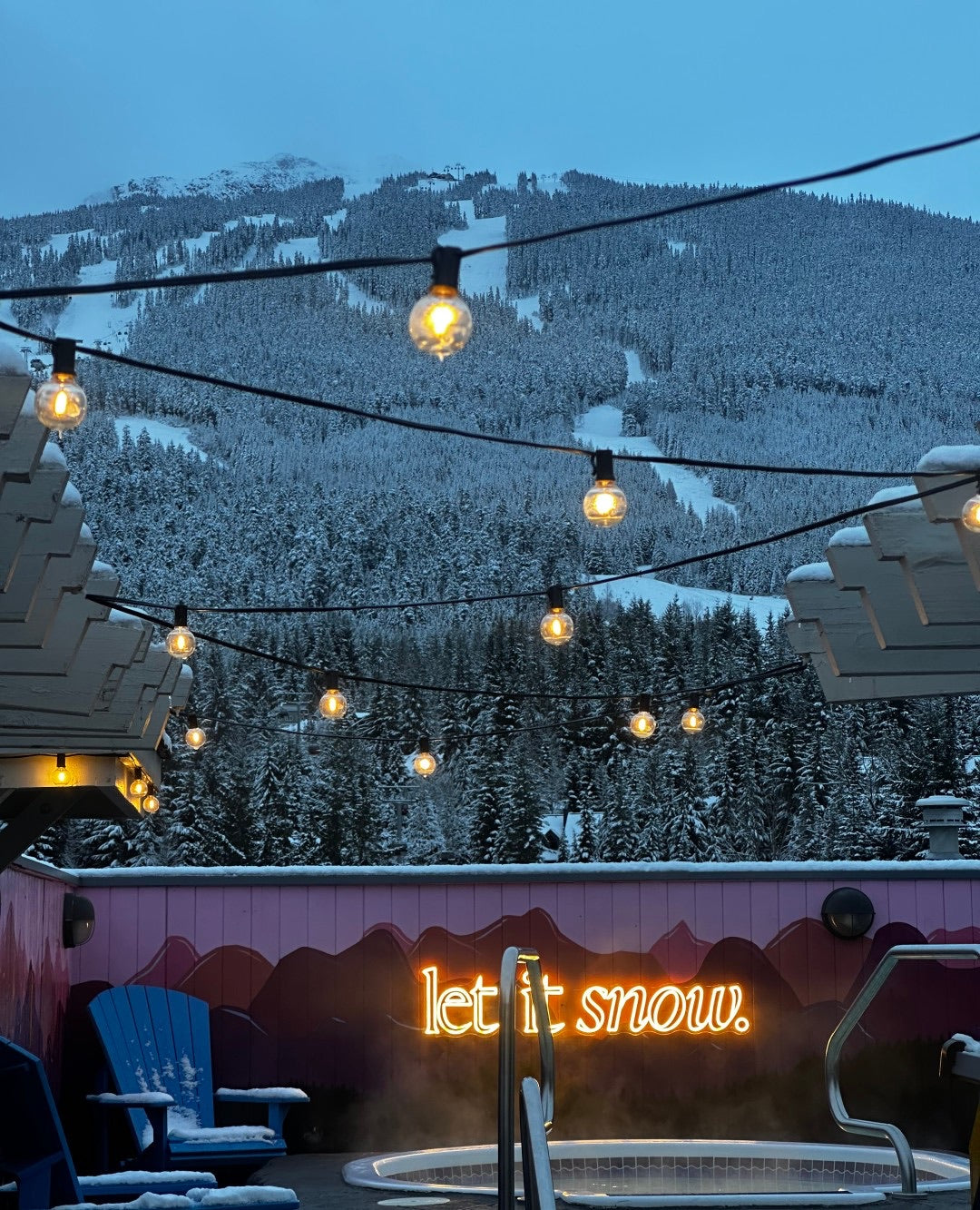 warm white neon sign saying let it snow by rooftop hot tub in whistler mountain