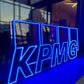 Neon sign with 'KPMG' logo in front of a glass building