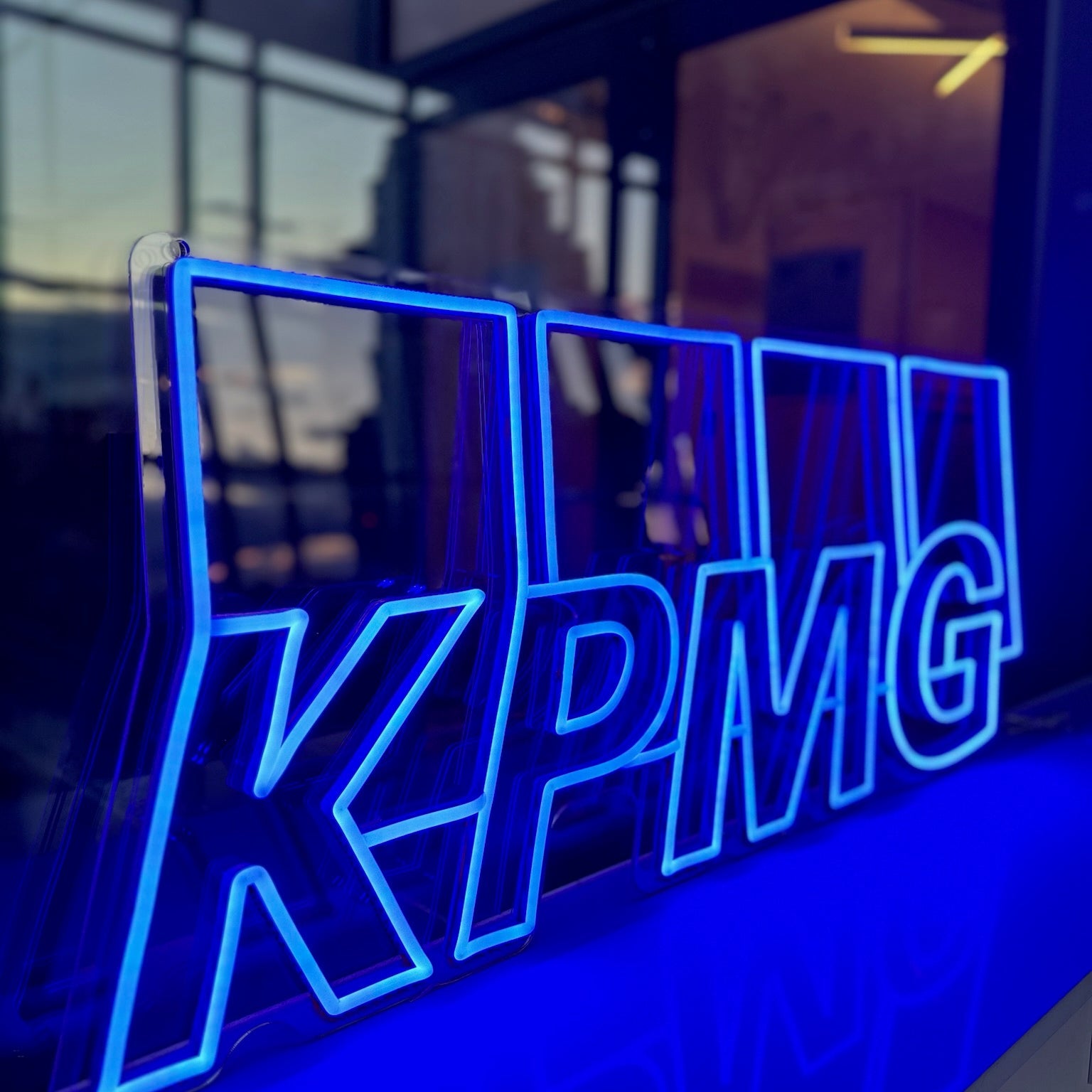 Neon sign with 'KPMG' logo in front of a glass building