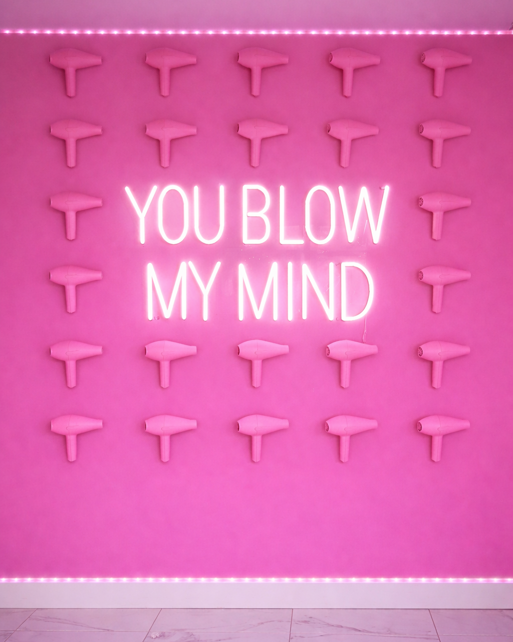 Pink wall with multiple hair dryers and a neon sign saying 'You Blow My Mind'.