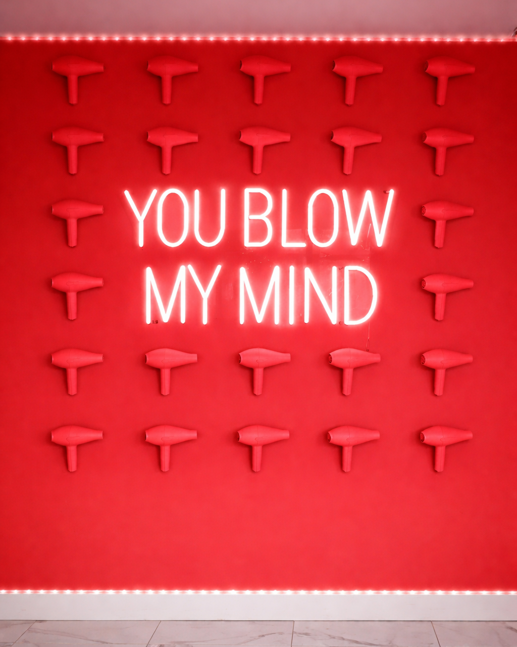 Neon sign with 'YOU BLOW MY MIND' text on a red wall with decorative elements.